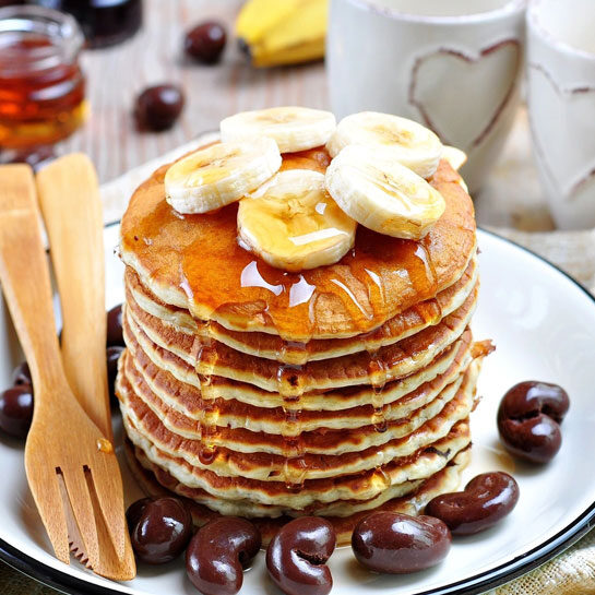 A plate of pancakes with bananas and maple syrup.