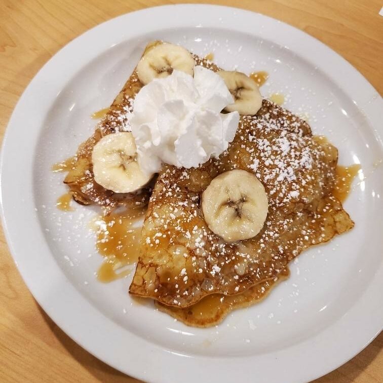 A white plate topped with pancakes covered in syrup and bananas.